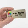 A hand holding a 1.5 x 3.5 Gold Name Tag